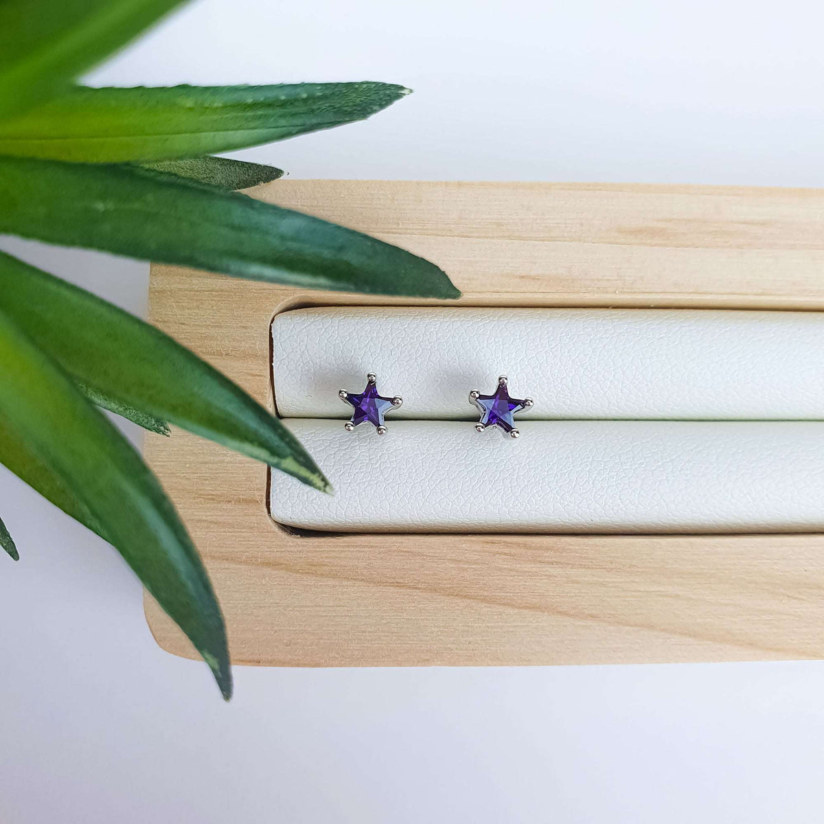 Sidabro atspalvio žvaigždžių smeigtukiniai auskarai su ryškiai violetiniais kristalais ant medinio padėklo