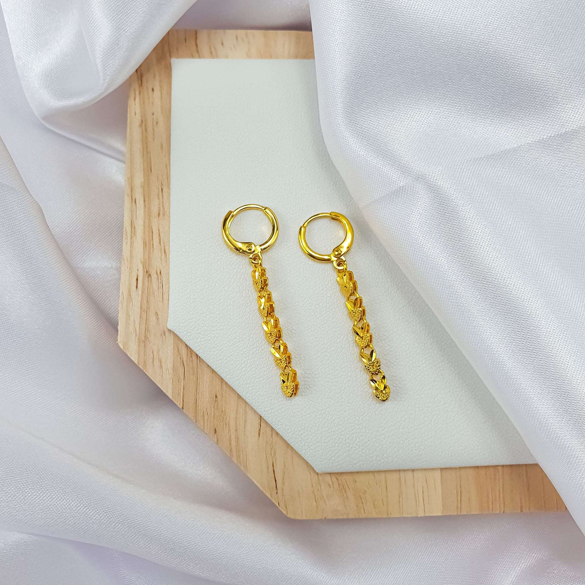 Ilgi širdelių auskarai ant medinio padėklo, matomas prancūziškas užsegimas ir auksinės grandys