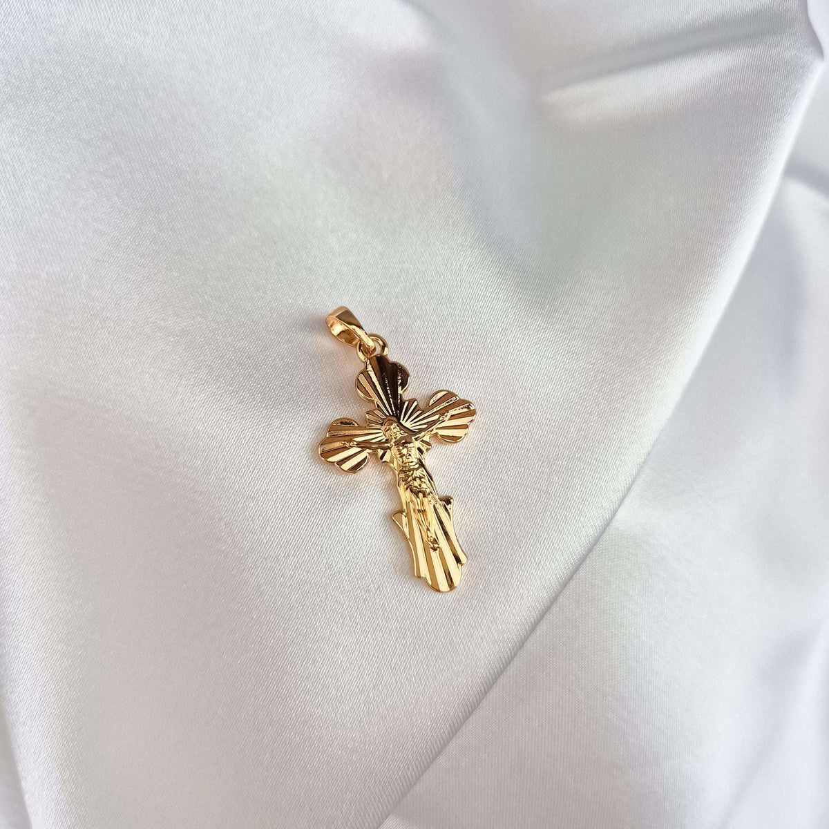 Paauksuotas stačiatikių kryželis su spindulių graviūra ir Kristaus figūra ant balto atlaso