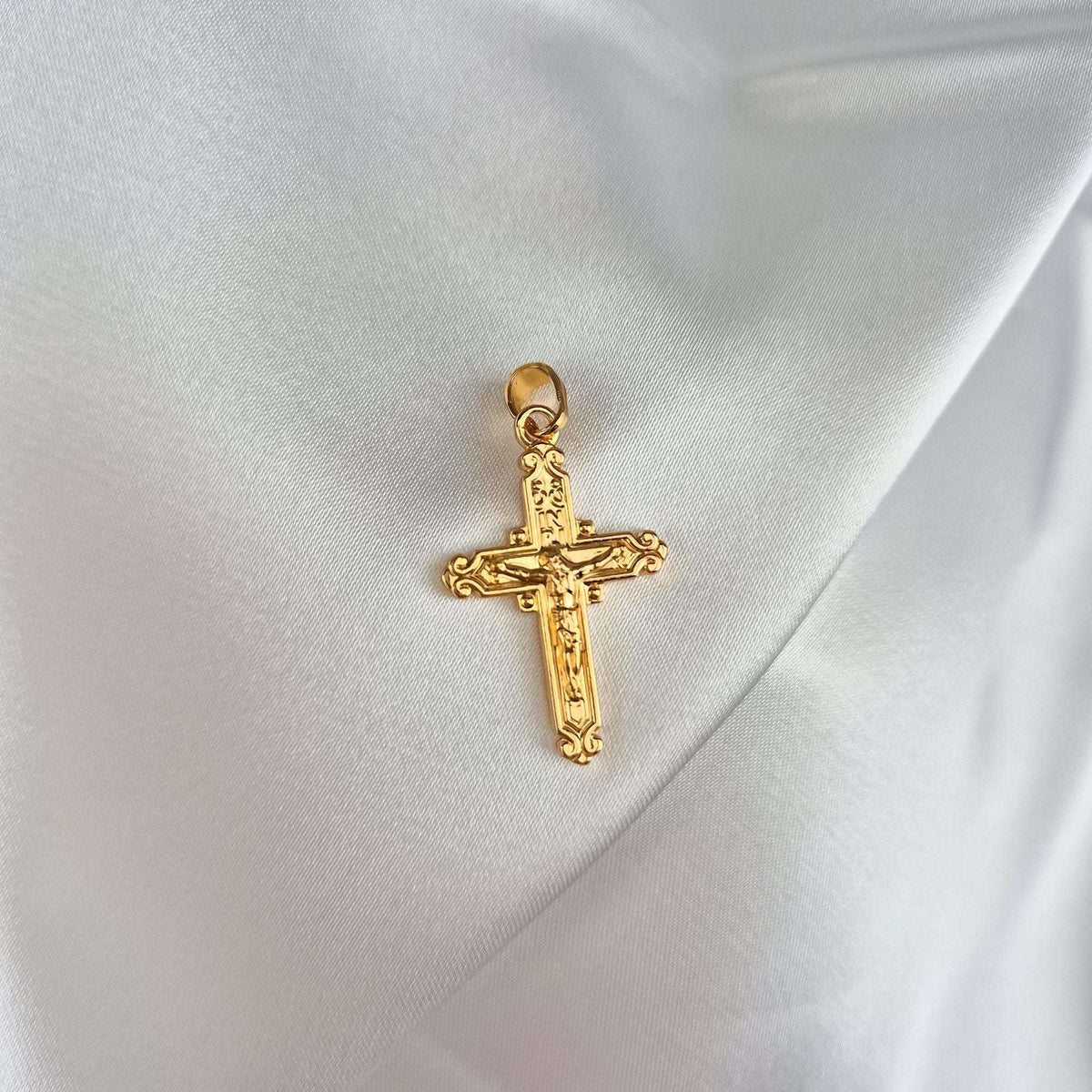 Paauksuotas katalikiško kryžiaus pakabukas su Kristaus figūra ir INRI užrašu ant balto atlaso