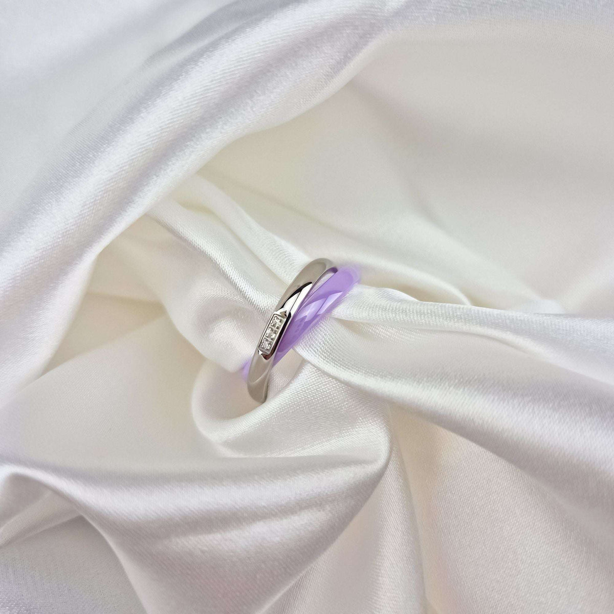 Violetinis keramikos žiedas su platinos danga stambiu planu ant balto šilko audinio klosčių