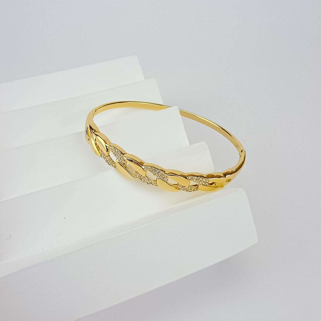 Paauksuota standi bangle apyrankė su grandinės grandžių raštu ir žėrinčiais cirkoniais ant balto postamento