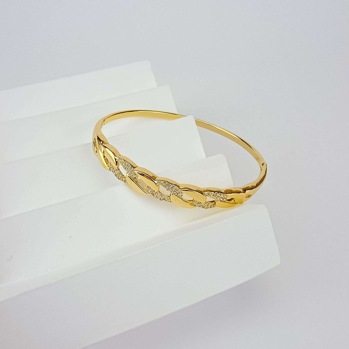 Paauksuota standi bangle apyrankė su grandinės grandžių raštu ir žėrinčiais cirkoniais ant balto postamento